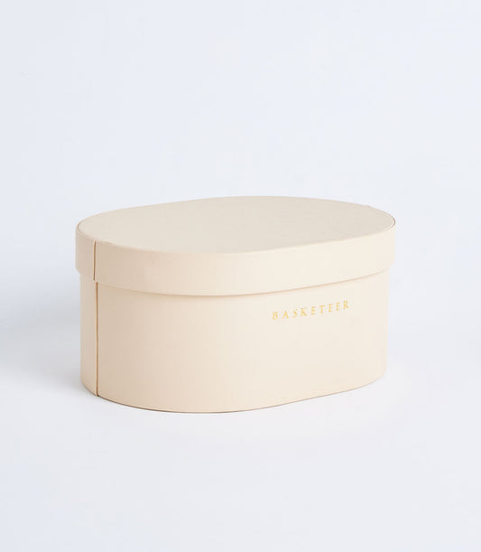 Beige round leather storage box with metallic gold Basketeer branding and removable lid