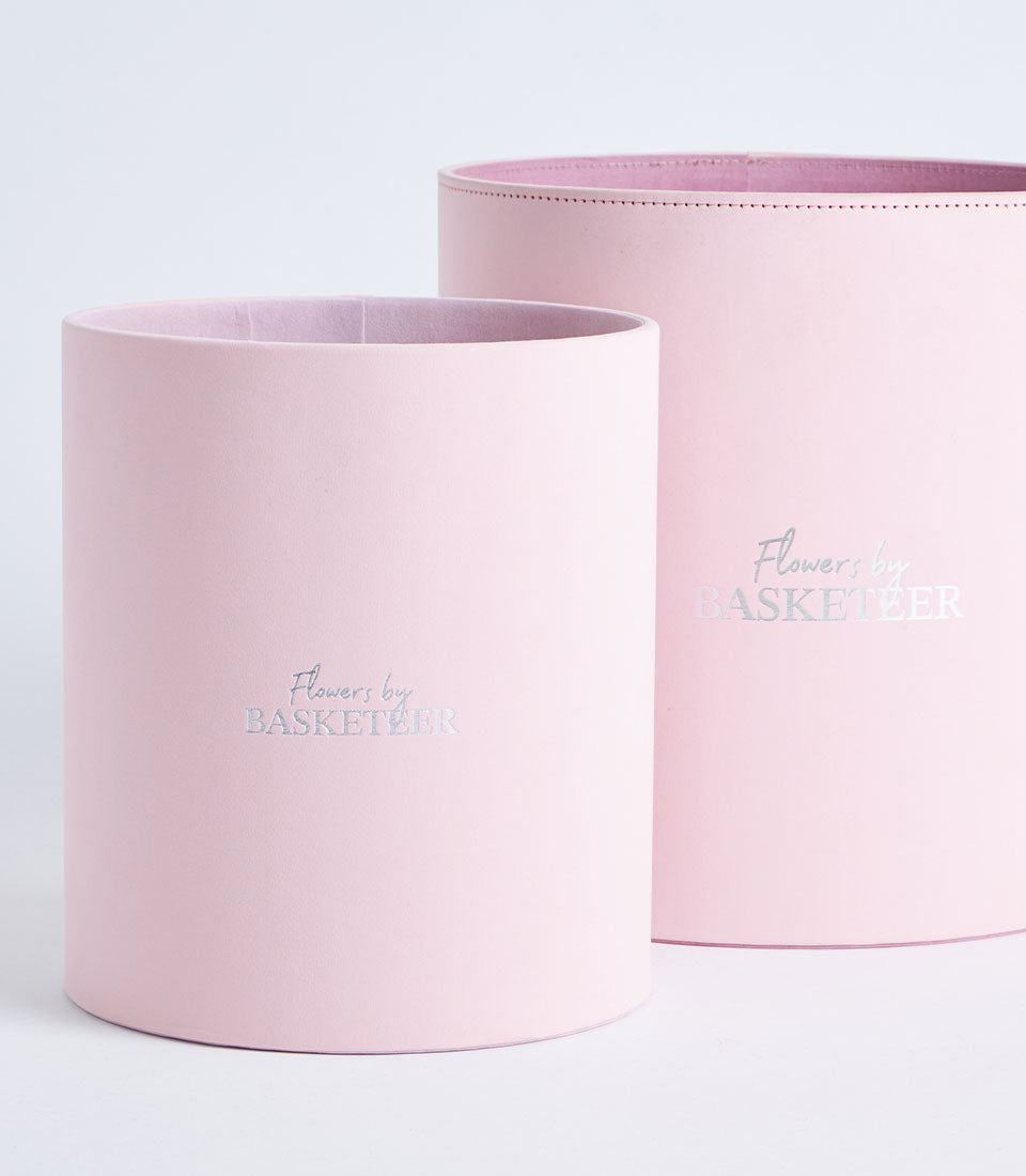 Two elegant blush pink round gift boxes, featuring "Flowers by Basketeer