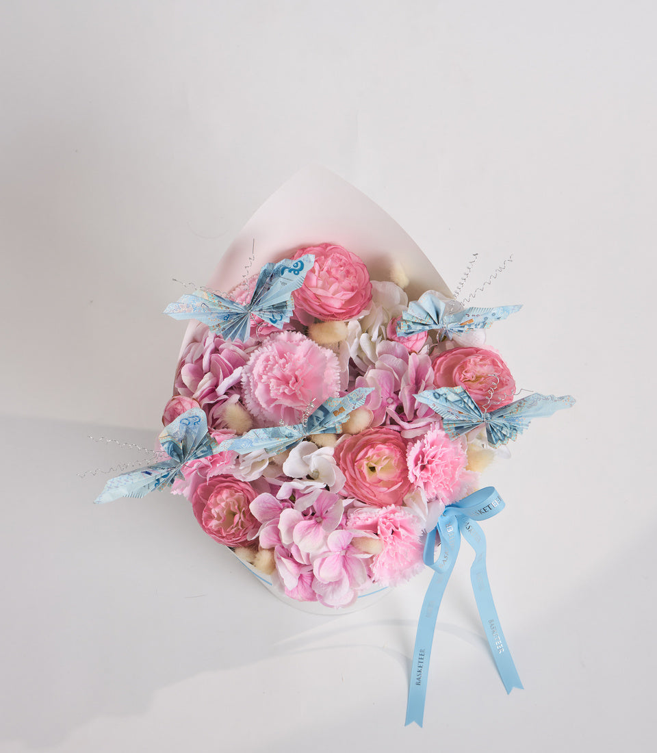 Luxurious floral gift arrangement with pink peonies and roses, blue butterfly decorations, cream wrapping, and blue ribbon bow on white background.