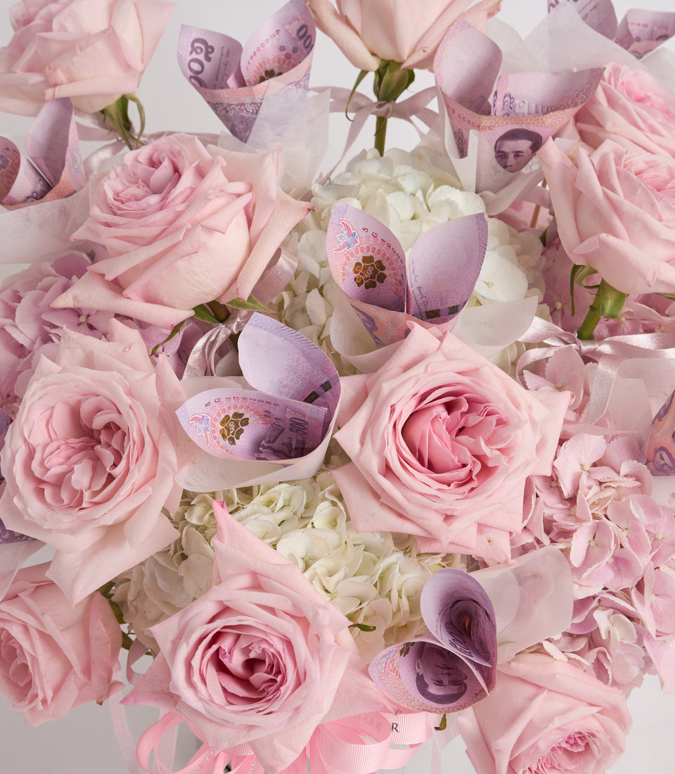 Luxury floral arrangement with pink roses, white hydrangeas, and decorative purple banknote-wrapped stems in elegant gift presentation.