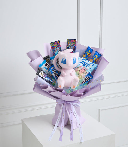 Pink plush Pokémon bouquet with candies, trading cards, and sweets arranged in lavender tissue paper with ribbon bow.