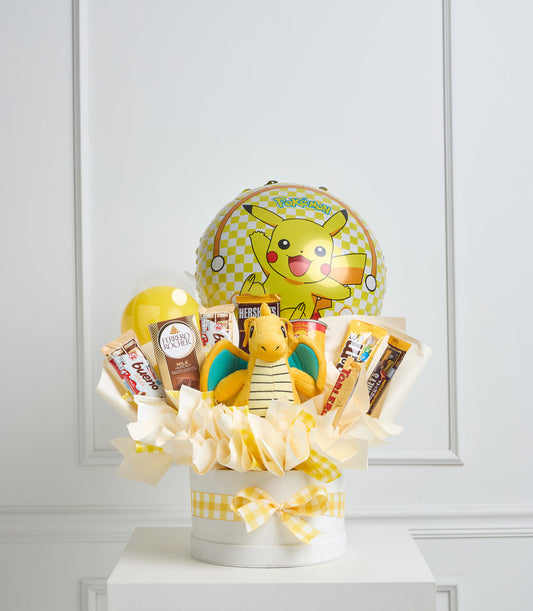 Yellow and white Pokémon gift basket with Pikachu balloon, plush Squirtle, chocolates, beauty products, and gingham ribbon bow on white pedestal.
