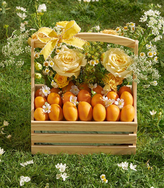 Luxury wooden crate with fresh apricots and vibrant yellow roses, white flowers, and green foliage with yellow ribbon bow