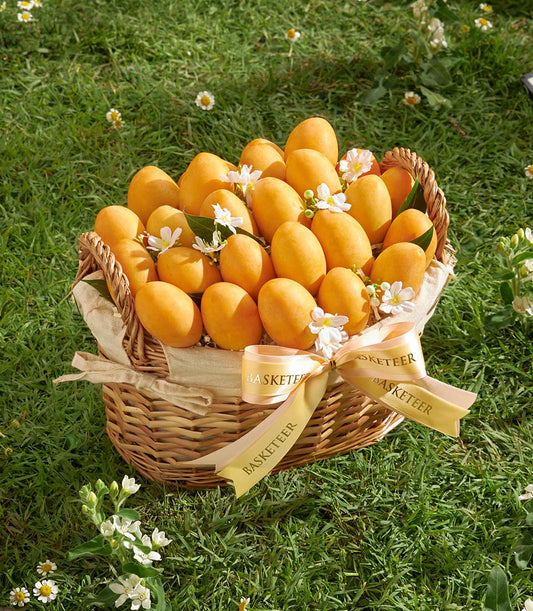 Golden wicker basket overflowing with ripe yellow mangoes, white flowers, and gold ribbon bow