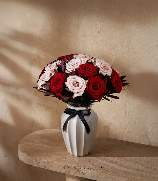 Red and light pink rose bouquet in white ceramic fluted vase with black ribbon