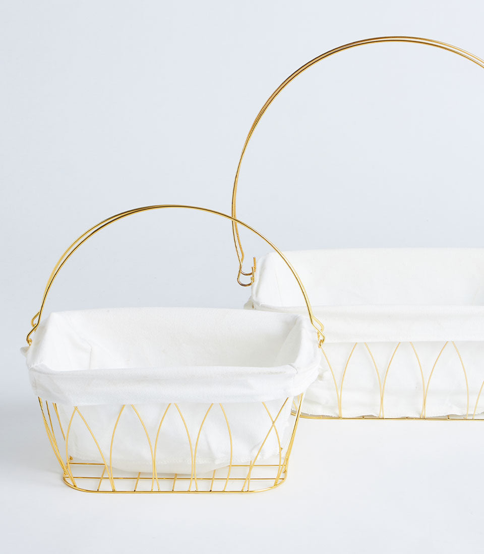 Gold wire baskets with white fabric liners and arched handles, perfect for elegant gift hampers and storage