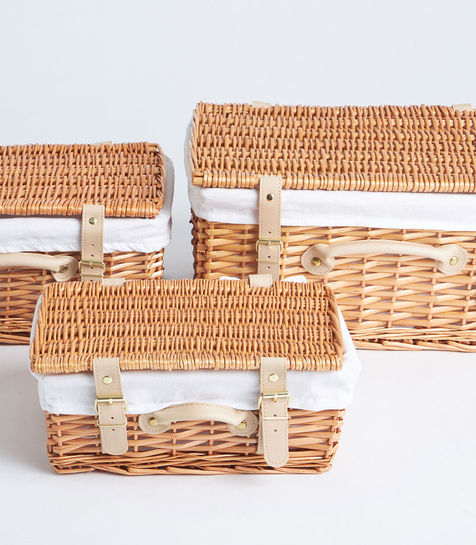 Natural woven picnic baskets in three sizes with cream linen lining and leather strap closures