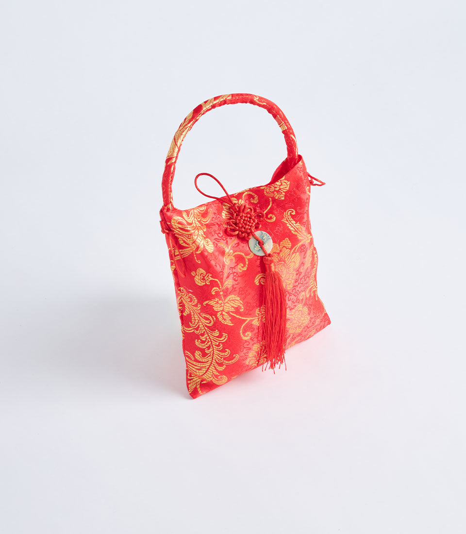 Red brocade fabric gift basket with gold floral patterns, tassel and decorative handle