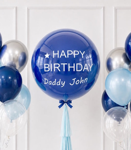 Blue bubble balloon with "Happy Birthday Daddy John" text, surrounded by silver and light blue balloons against white paneled wall.
