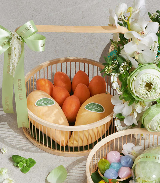 Songkran gift set with fresh Nam Dok Mai mangoes, orchids, lotus flowers, and pastel Thai desserts in wooden baskets