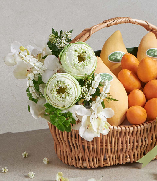 Wicker gift basket with premium yellow mangoes, citrus fruits, and light green lotus buds with white orchids