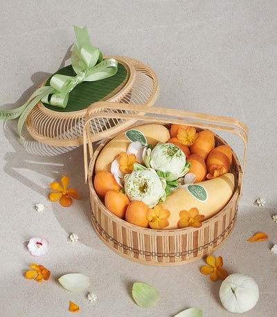 Woven bamboo gift basket with Nam Dok Mai mangoes, tropical fruits, white lotus buds, and fresh flowers tied with green