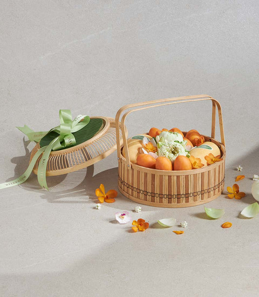 Songkran Scented Bliss gift basket with tropical fruits, white lotus flowers, and orange orchids in woven bamboo