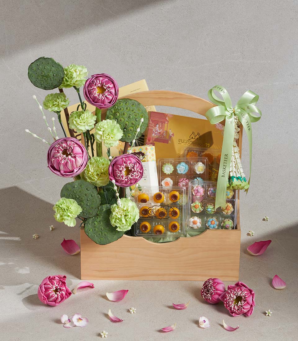 Light wooden gift basket with Thai desserts, pink lotus flowers, and green foliage arranged for Songkran gifting