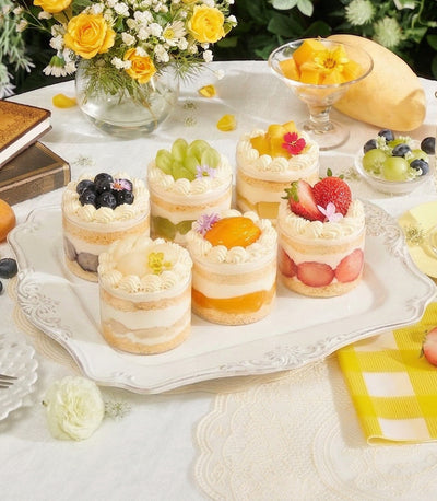 Six mini chiffon cakes with fresh cream and assorted fruits in elegant clear containers on ornate serving tray
