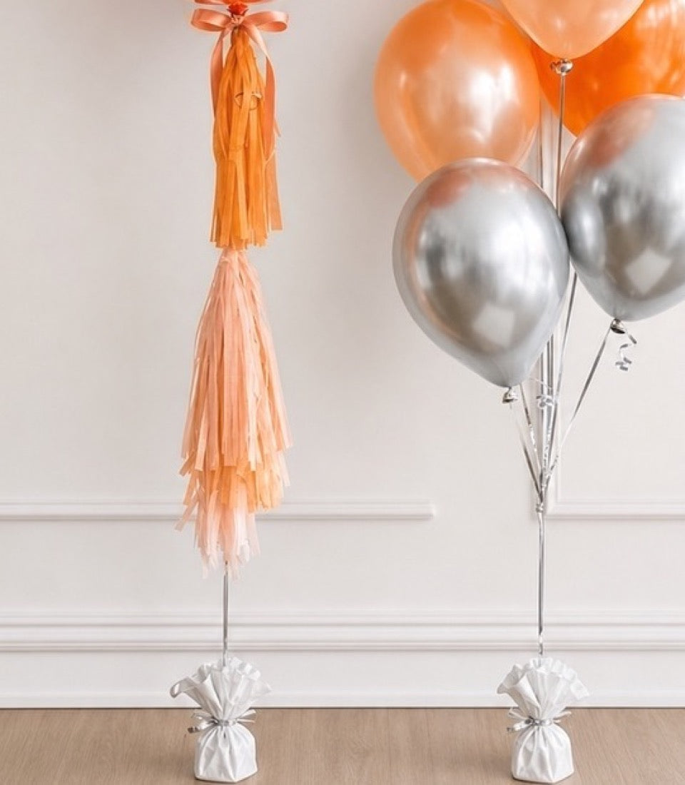 Elegant balloon decorations featuring peach and silver metallic balloons with matching tassel garland and weighted bases.