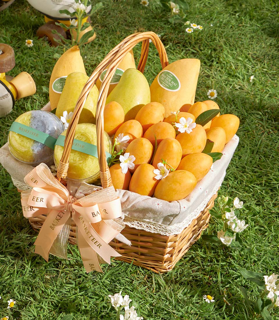 Woven wicker gift basket with Thai mangoes, mayongchid fruits, sticky rice, and tied with pink ribbon bow