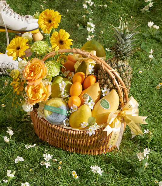 Premium tropical fruit gift basket with fresh mangoes, pineapple, and pears, accented with yellow gerbera daisies and orange