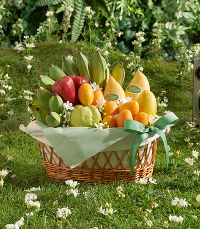 Woven wicker basket overflowing with fresh Thai mangoes, bananas, and seasonal fruit tied with green ribbon