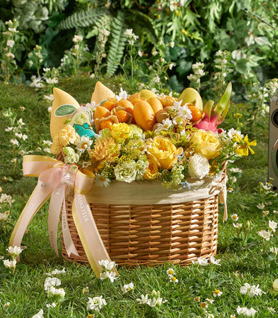 Woven wicker fruit basket with fresh mangoes, dragon fruit, and yellow roses, tied with pale yellow ribbon