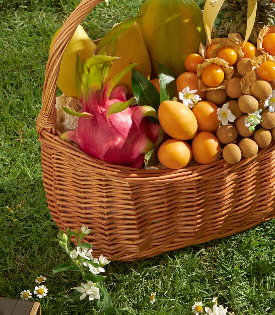Luxury wicker basket filled with fresh Thai tropical fruits including dragon fruit, mangoes, papaya, longans and physalis