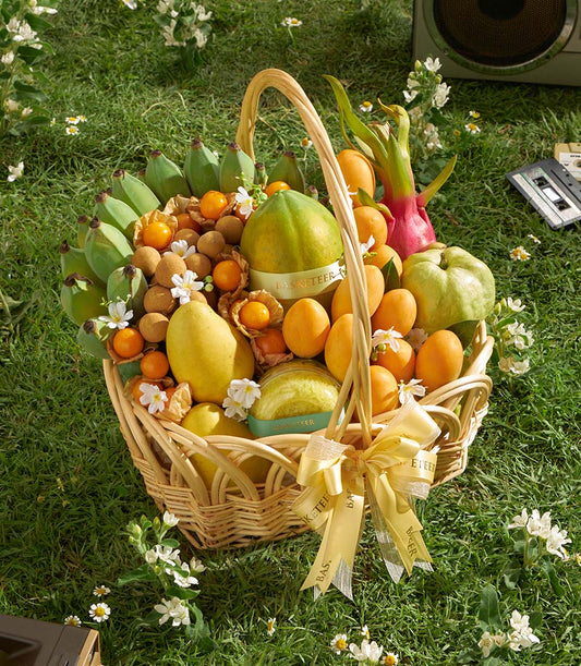 Woven wicker basket overflowing with fresh Thai tropical fruits including mango, papaya, longan, and guava on green grass
