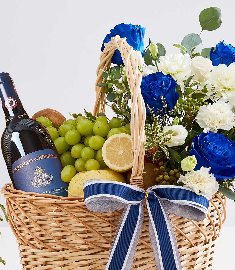 Luxury wicker gift basket with red wine, fresh fruit, and blue roses with white dahlias for anniversaries