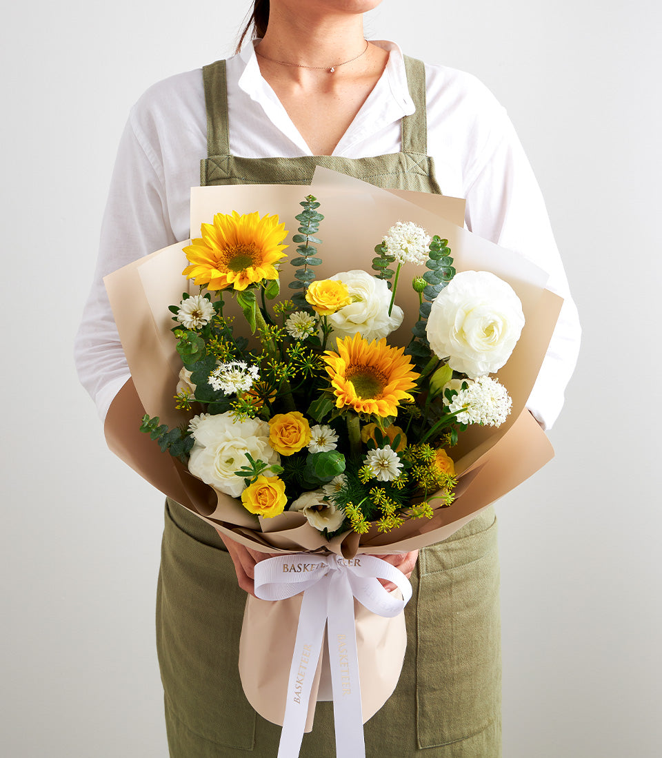 Vibrant sunflower bouquet with white ranunculus, yellow spray roses, and eucalyptus,