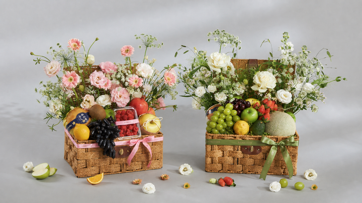 Two premium Basketeer fruit baskets with fresh flowers and assorted fruits on a soft gray studio background, luxury gift baskets for delivery in Bangkok.