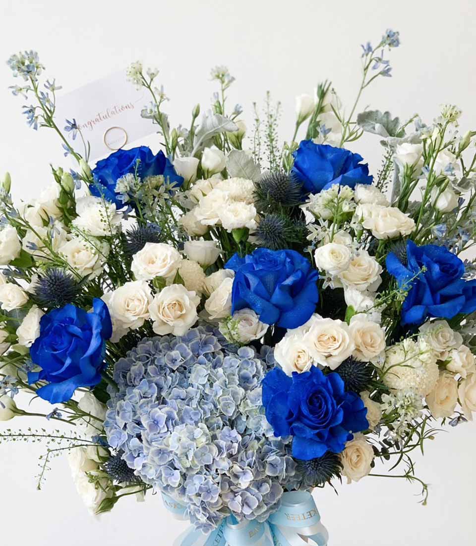 Premium blue and white floral arrangement with roses, hydrangeas, and thistles in a gift vase