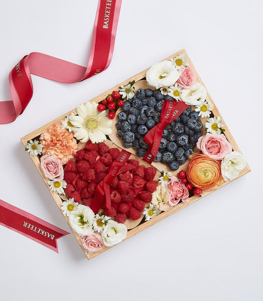 Wooden gift box with fresh raspberries and blueberries, artisan flowers, red ribbon