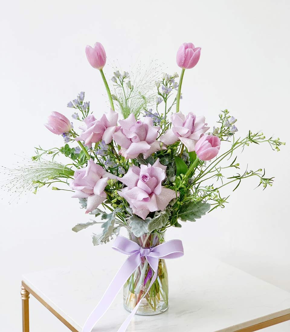Lavender roses and pink tulips fresh flower bouquet in glass vase with purple ribbon