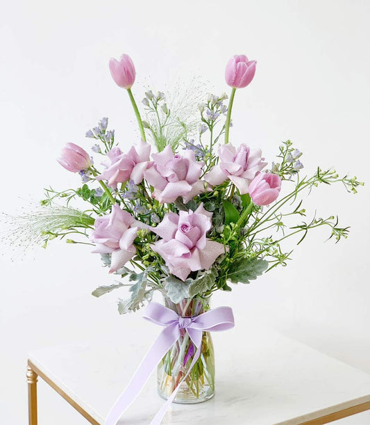 Lavender roses and pink tulips fresh flower bouquet in glass vase with purple ribbon