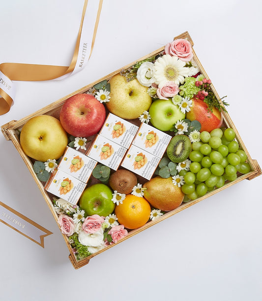 Wooden tray with fresh pears, apples, grapes, kiwis, gourmet treats, and pink roses on white background
