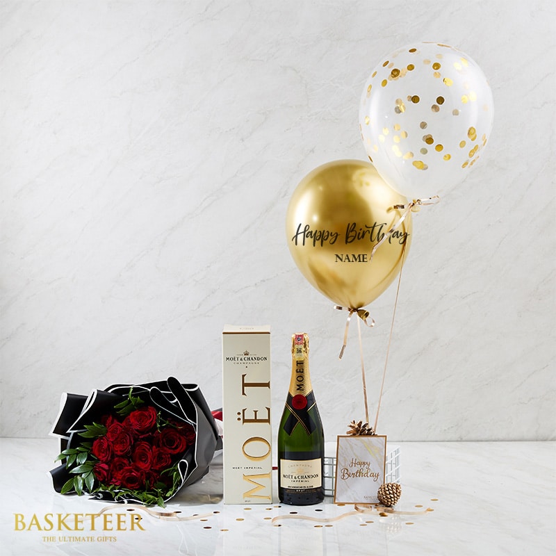Luxury Moët champagne gift set with deep red roses, gold confetti balloons, and birthday card on white marble