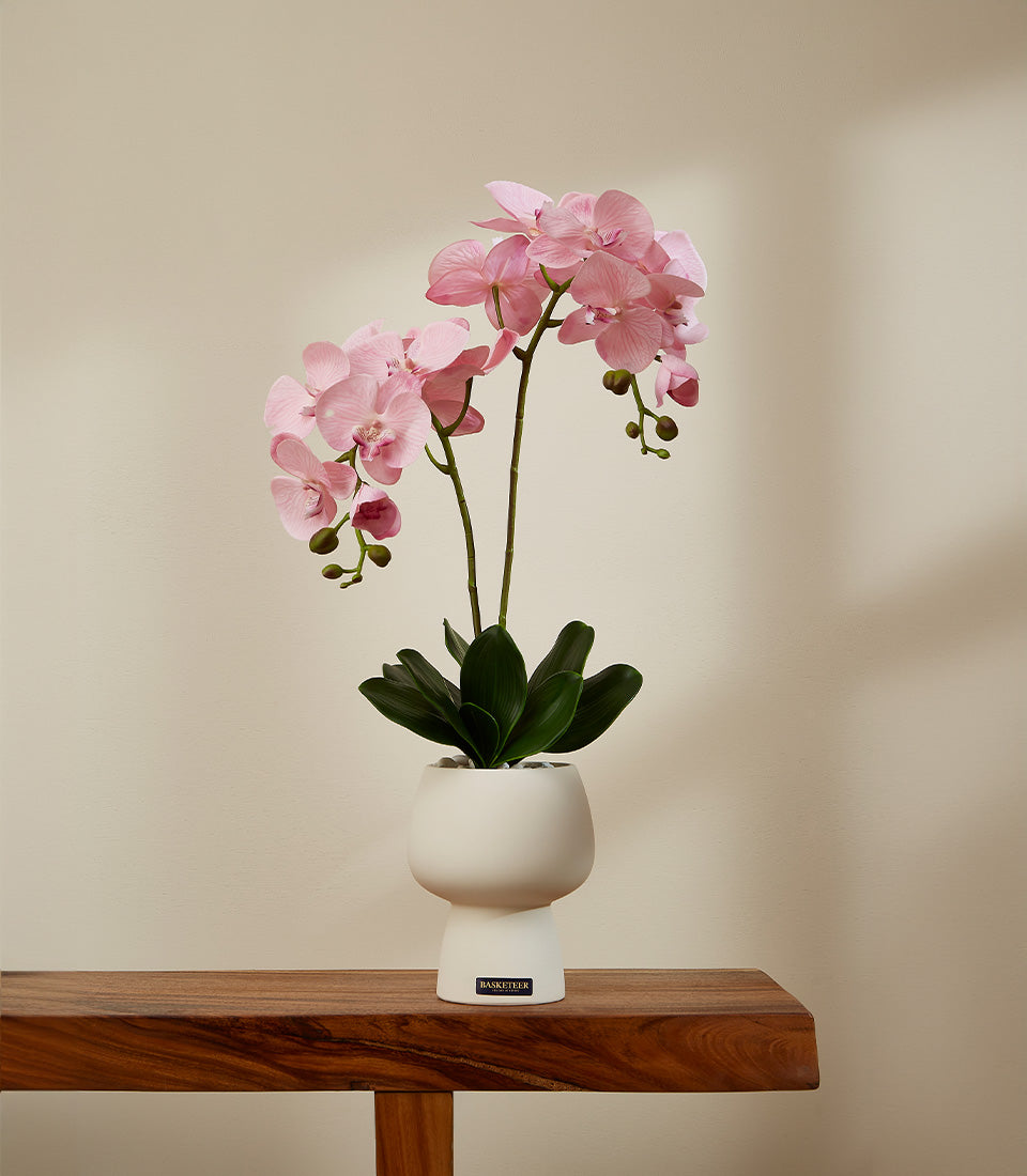 Faux pink orchid arrangement in white ceramic pot with decorative stones