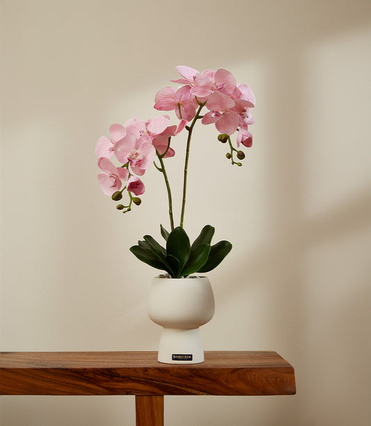 Faux pink orchid arrangement in white ceramic pot with decorative stones