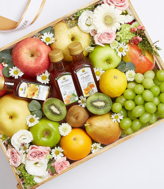 Wooden gift box filled with fresh apples, pears, kiwis, citrus fruits, grapes, honey bottles and white and pink roses