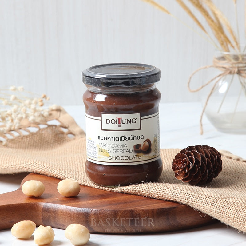 Doi Tung chocolate macadamia nut spread in glass jar with scattered nuts on wooden board