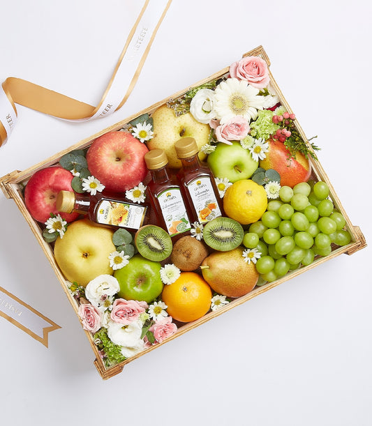 Premium wooden crate with fresh apples, pears, grapes, kiwis, citrus fruits, artisan cordials and fresh flowers
