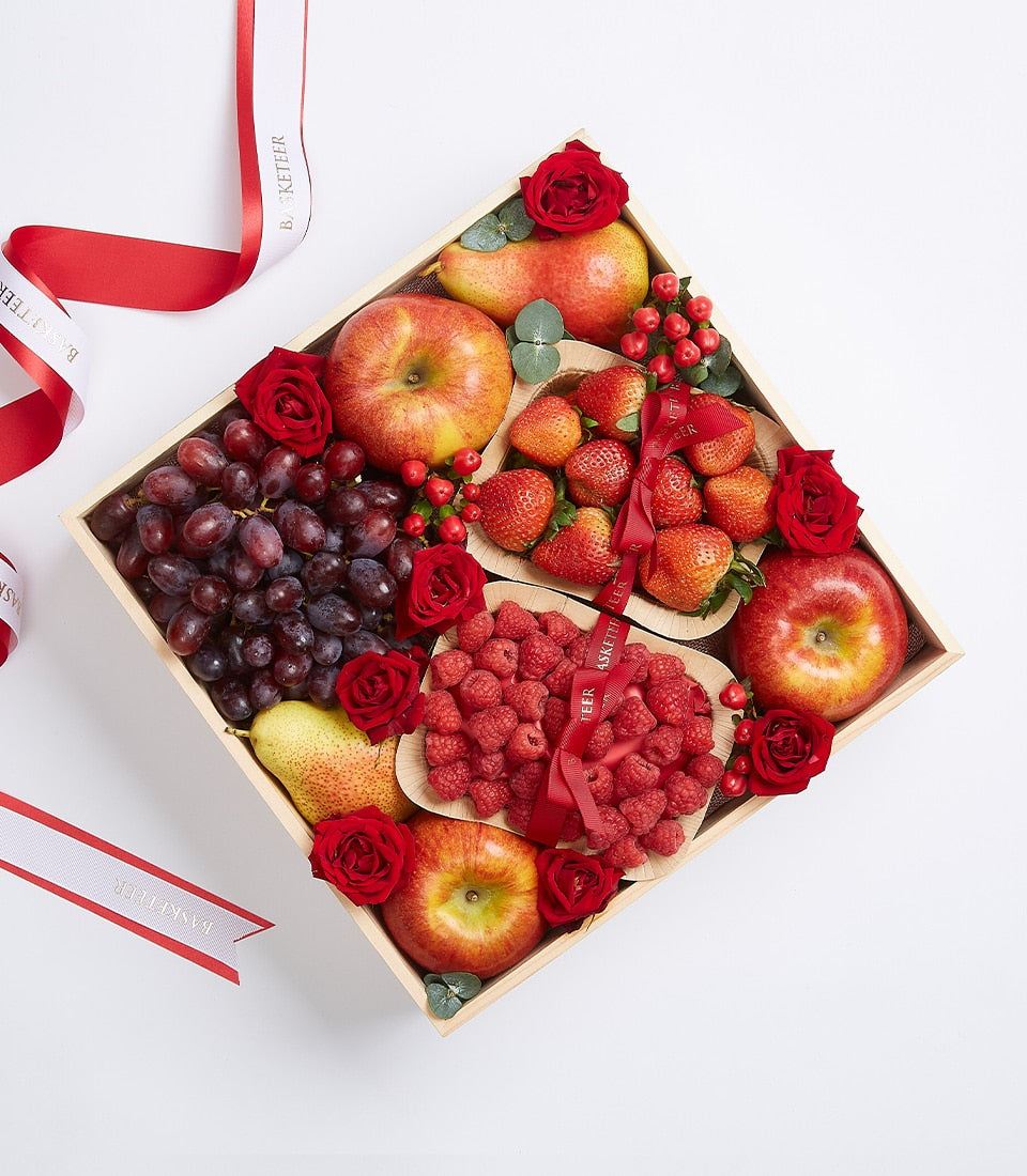 Premium fruit gift box with apples, grapes, strawberries, and pears nestled with red roses in light wood crate