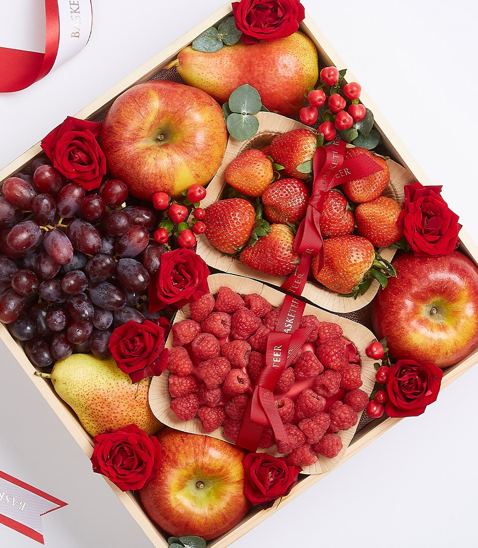 Wooden gift box with fresh apples, pears, grapes, strawberries, raspberries, and red roses