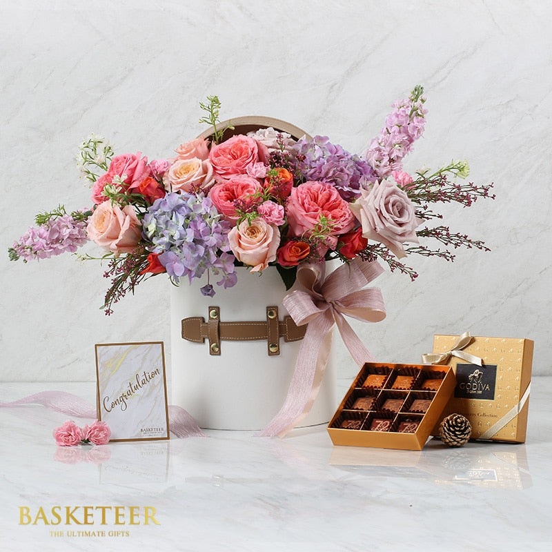 Luxury flower hatbox with pink roses, hydrangeas, and purple stock paired with artisan chocolates in gold gift box