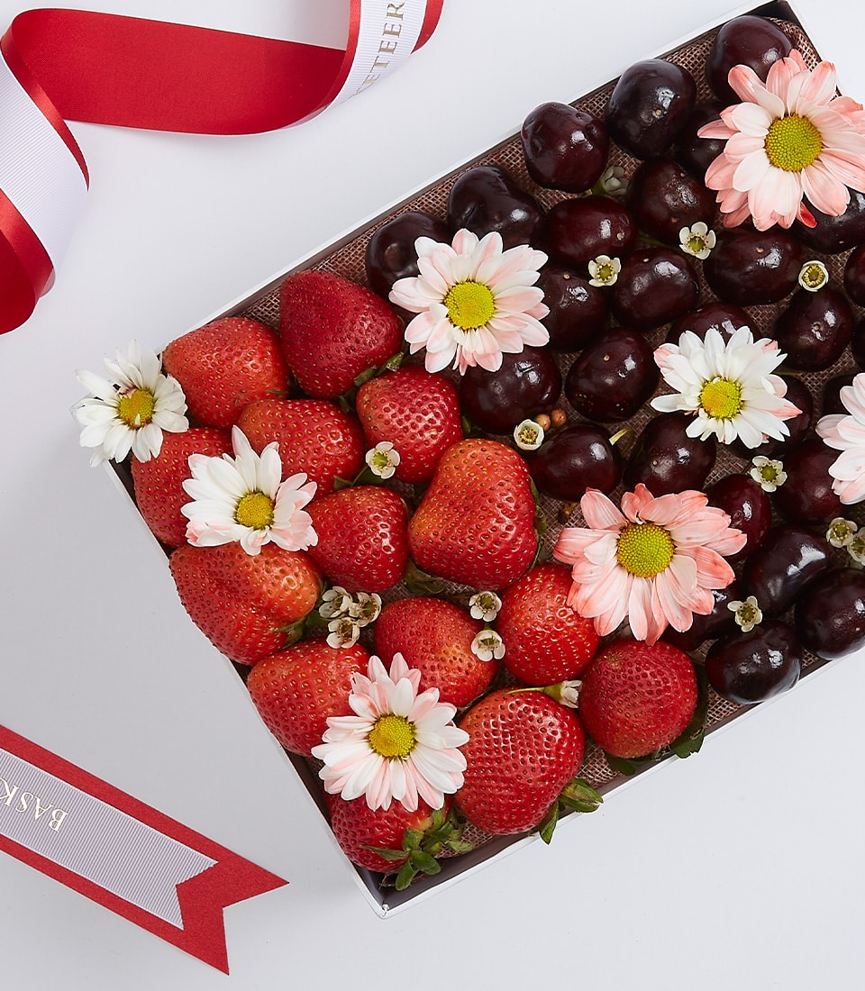 Heart-shaped fruit gift box with strawberries, cherries, and fresh flowers with red striped ribbon
