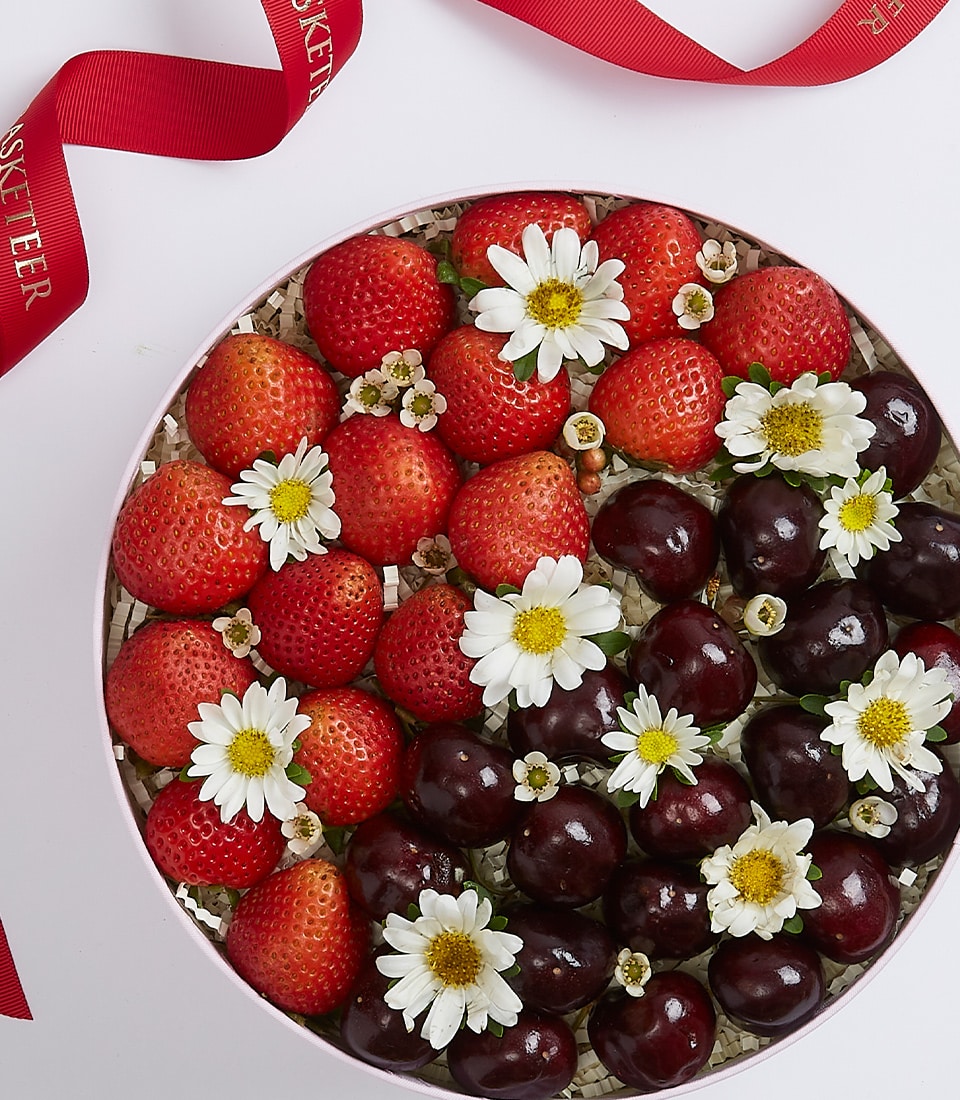 Fresh strawberries and cherries in light pink luxury gift box with white flowers and ribbon