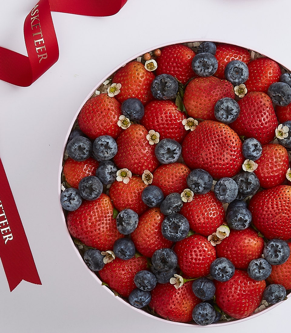 Luxury berry gift box with fresh strawberries, blueberries, and white flowers in pale pink packaging