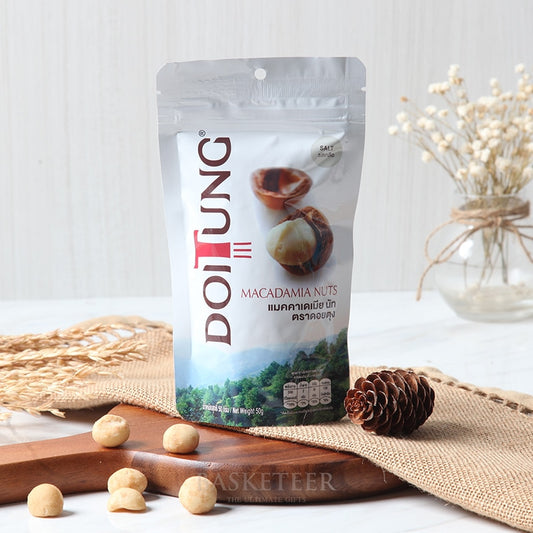 Doi Tung macadamia nuts salt flavour in white pouch with scattered nuts on wooden board