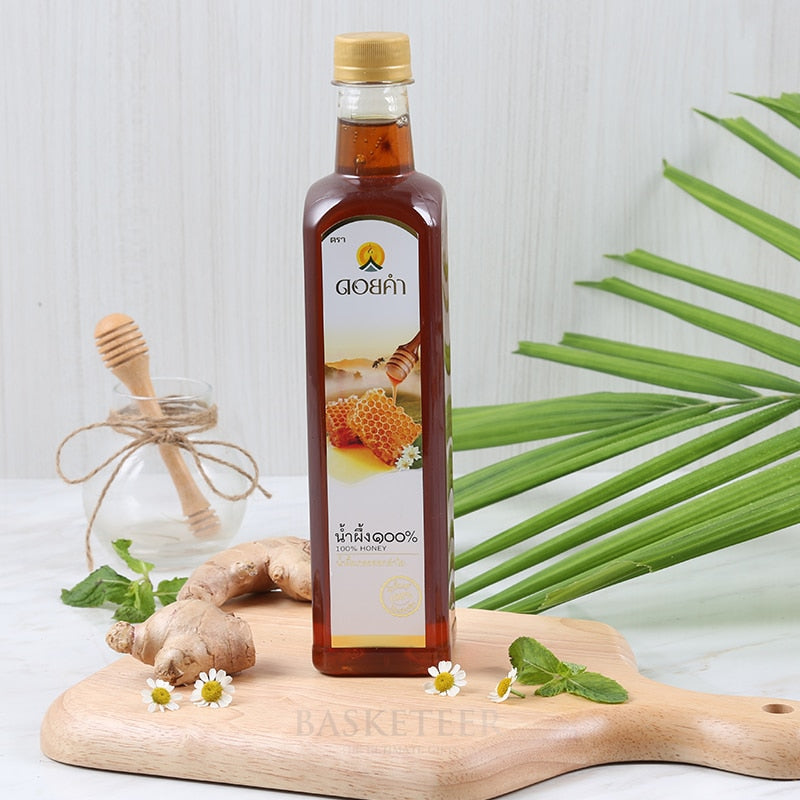 Pure amber honey in glass bottle with gold cap, styled with fresh ginger, mint, and daisies for artisan gift presentation