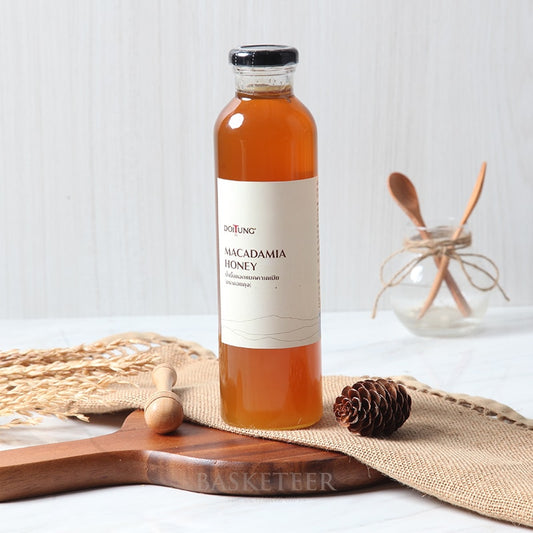 DoiTung macadamia honey in amber glass bottle with black cap on rustic burlap and wood