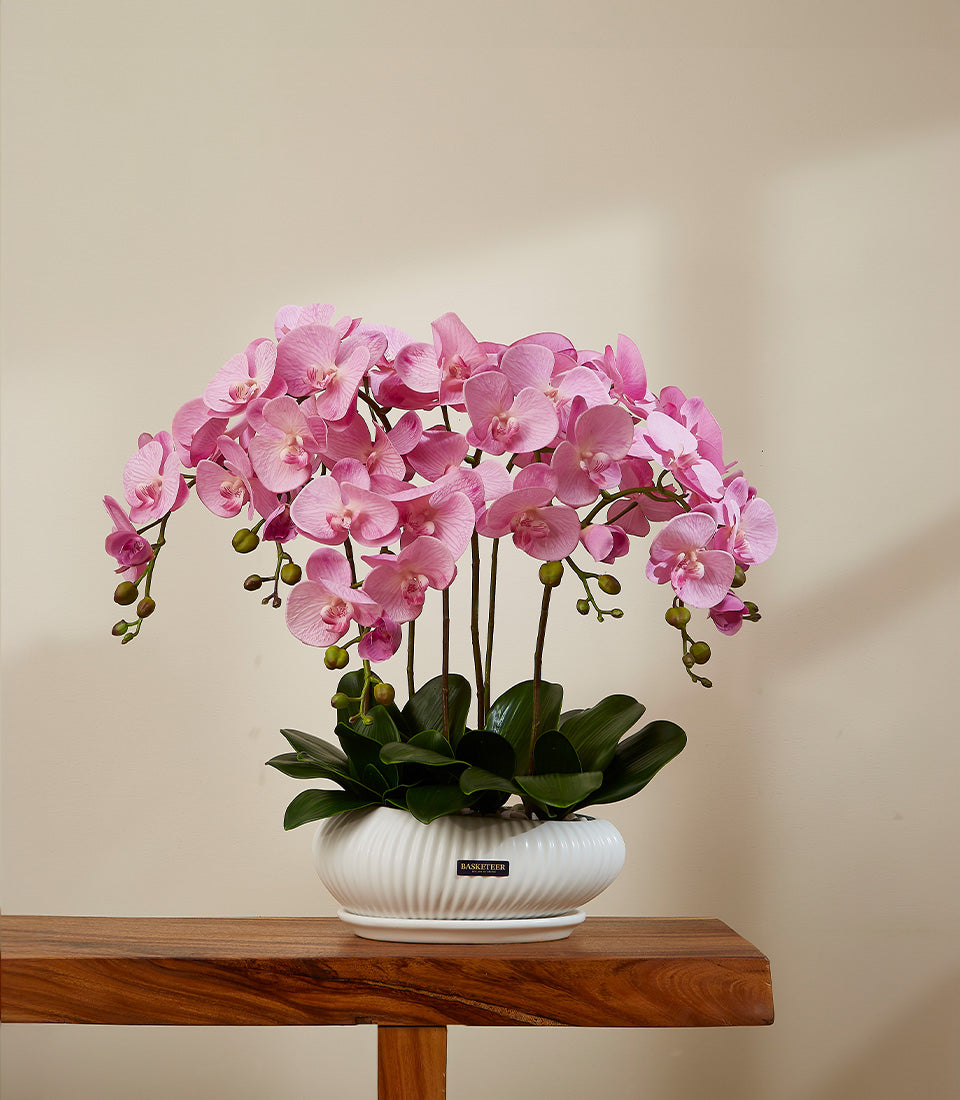 Vibrant pink artificial orchid arrangement in white ribbed ceramic planter with green leaves and saucer
